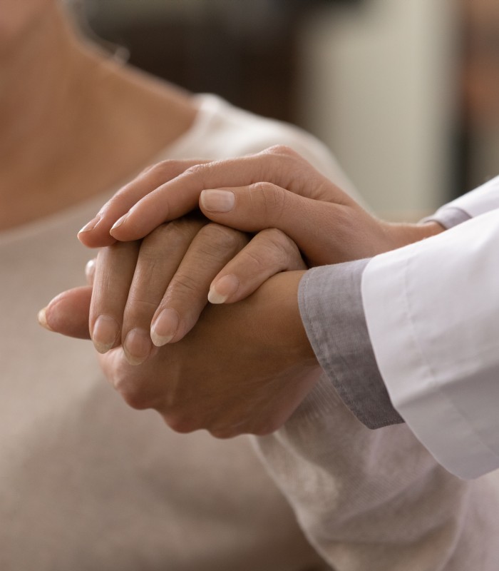 Close-up of a doctor holding a patient's hand in a comforting gesture.